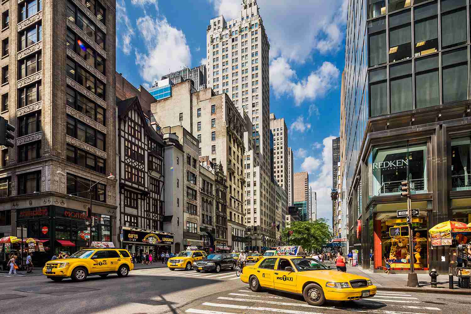 Busy Midtown Manhattan street in NYC with yellow taxis and tall buildingsv