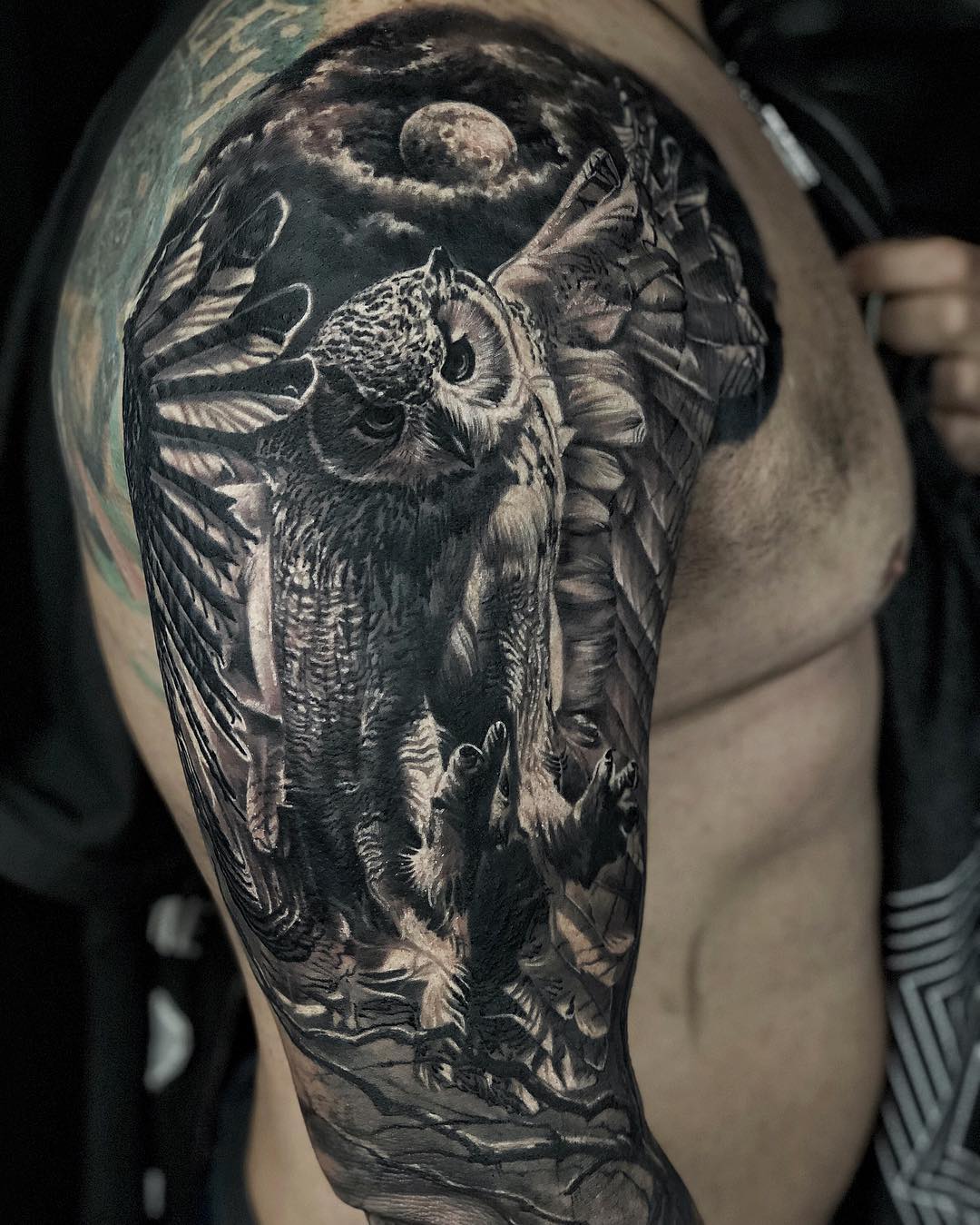 Black and grey realism owl tattoo on upper arm with wings spread under a moon, symbolizing wisdom and intuition