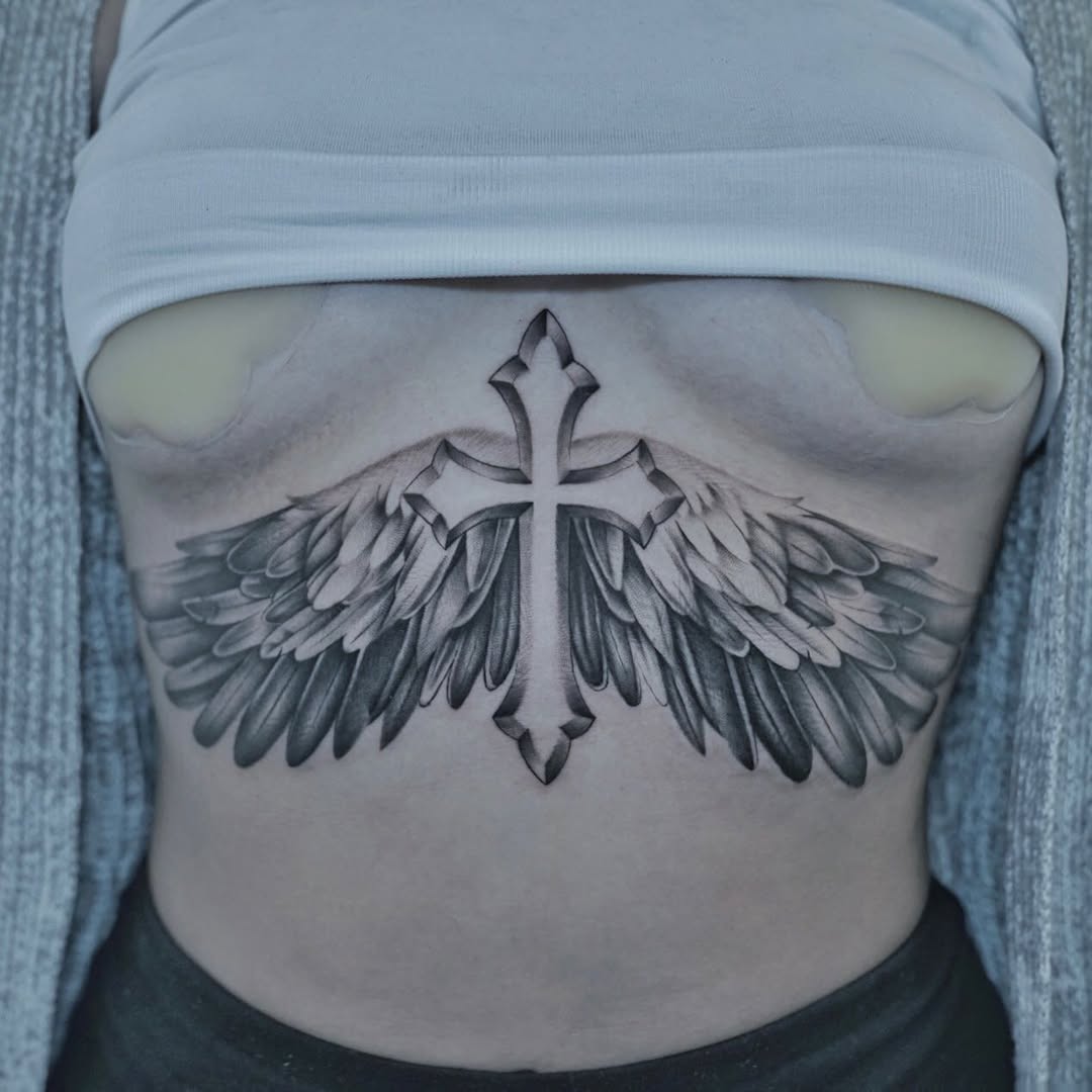 Black and grey realism cross tattoo with angel wings on chest, symbolism of faith and protection, Inknation Studio NYC