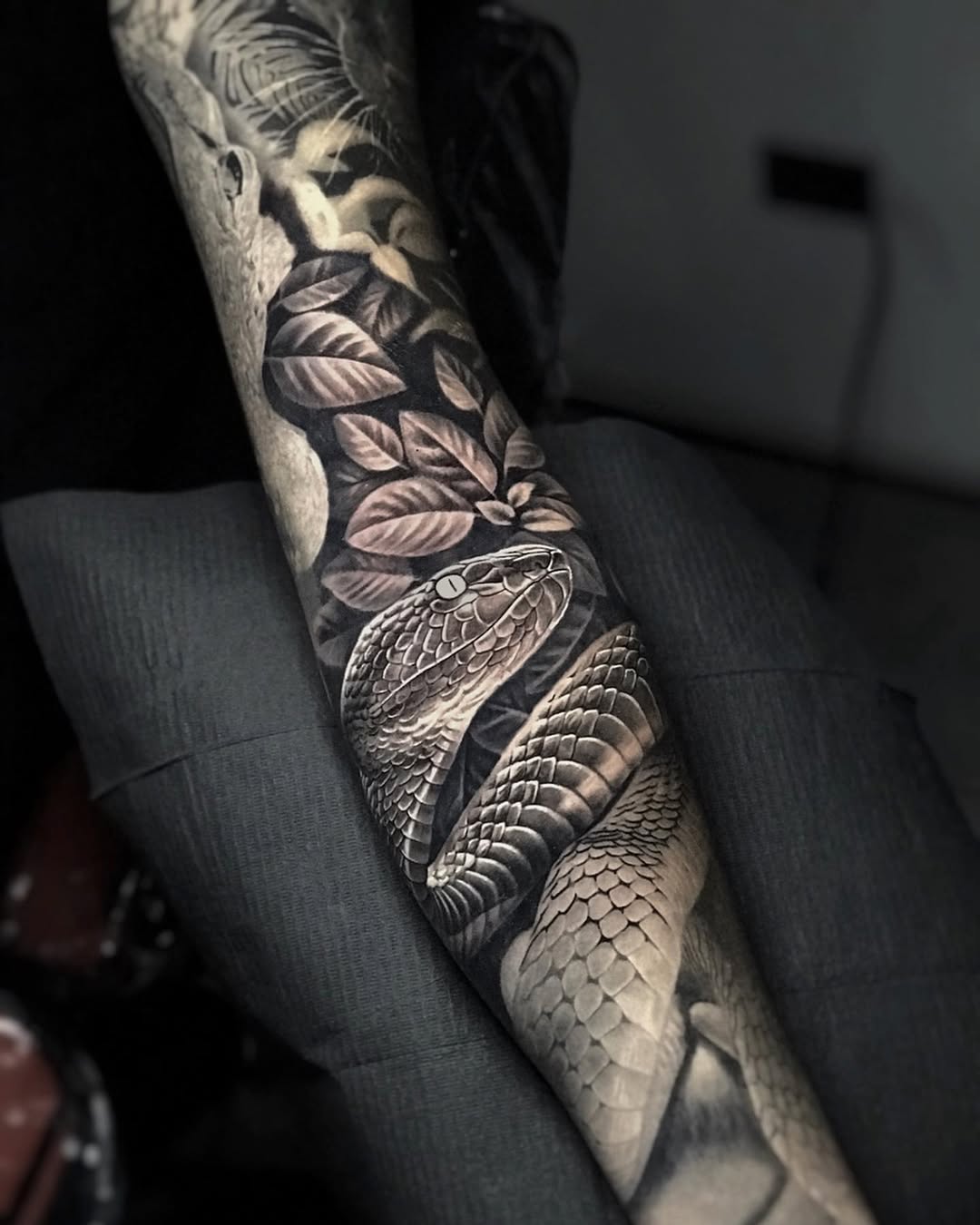 Black and grey realism python snake tattoo on upper arm with foliage, Inknation Studio NYC