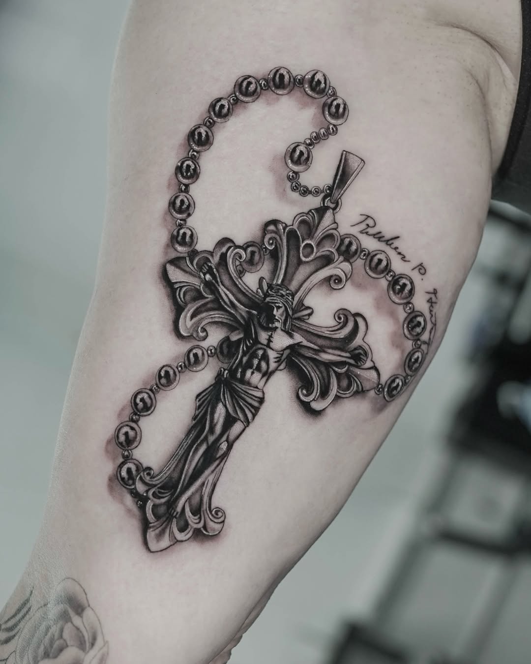 Black and grey rosary crucifix tattoo with Jesus on forearm, detailed realism, Inknation Studio NYC