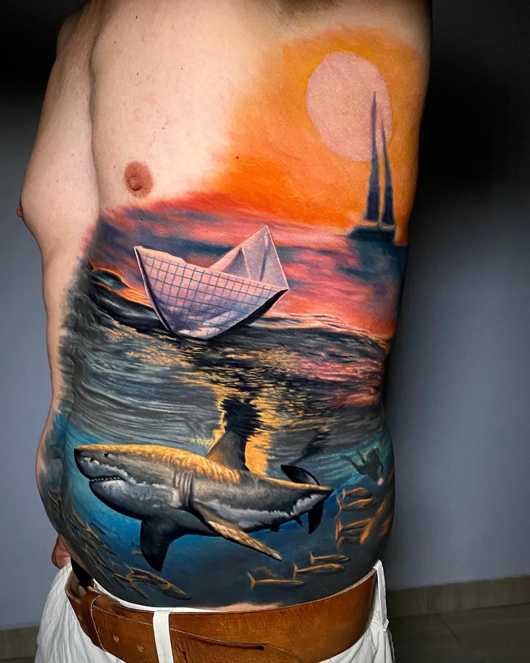 Large color realism great white shark tattoo on chest ribcage with paper boat and sunset ocean, Inknation Studio