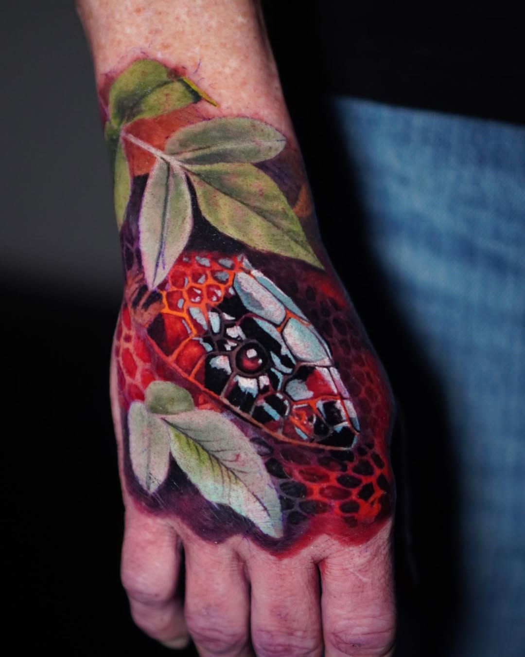 Color realism snake hand tattoo with red honeycomb scales and green leaves, transformation symbolism, Inknation Studio NYC