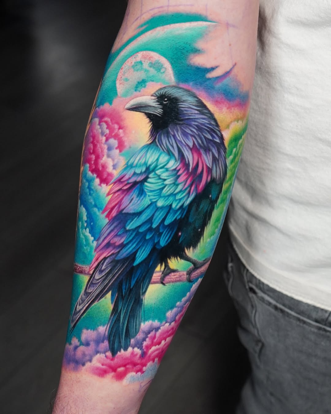Colorful realistic raven tattoo on arm with moon, vibrant clouds and galaxy background – modern raven bird tattoo ideas, Inknation Studio New York