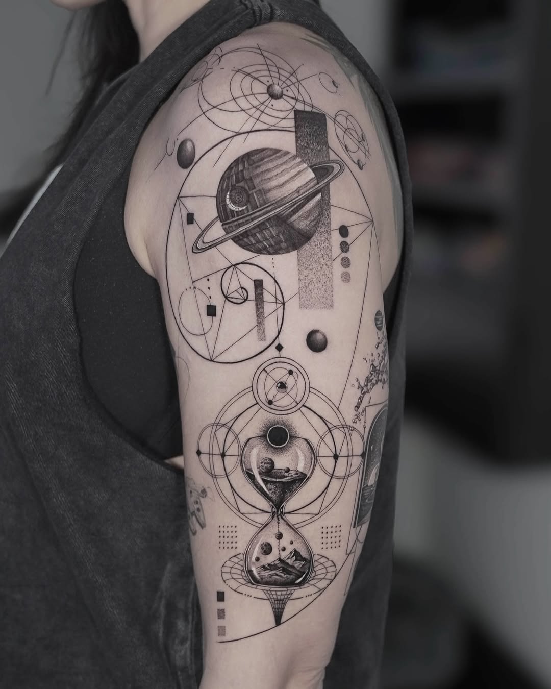 Geometric black and grey hourglass tattoo with cosmic planets and sacred geometry on upper arm, Inknation Studio