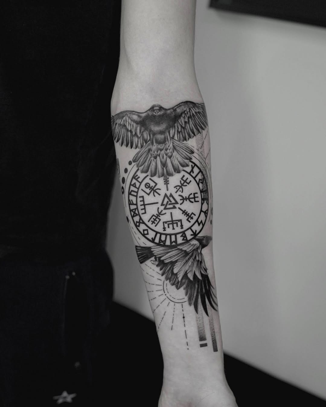 Black and grey nordic raven tattoo on forearm with Viking runes and Vegvisir compass, symbolizing wisdom and protection | Inknation Studio New York City