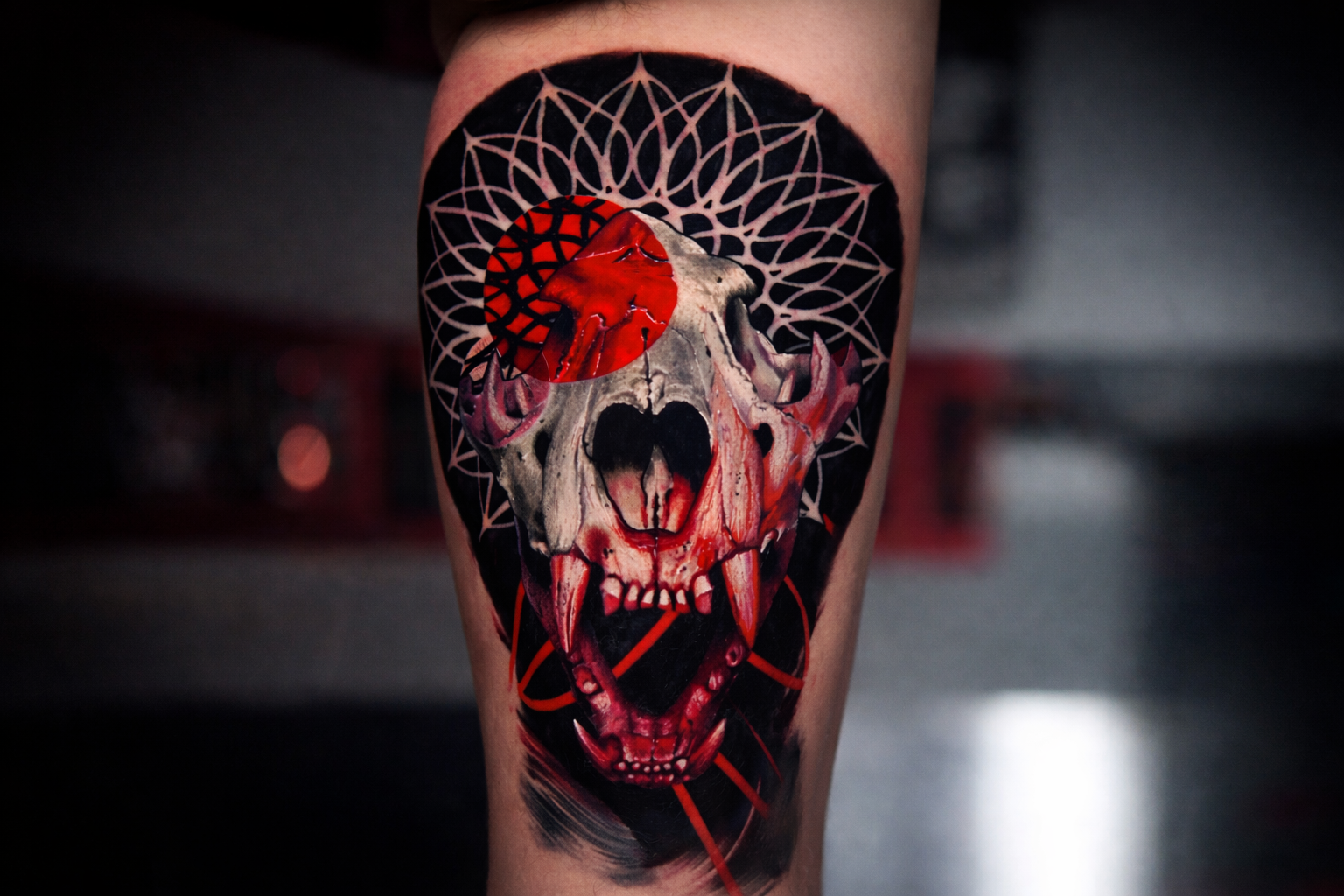 Trash polka skull tattoo with red ink accents and geometric mandala background on calf, bold black and red realism design in NYC tattoo studio